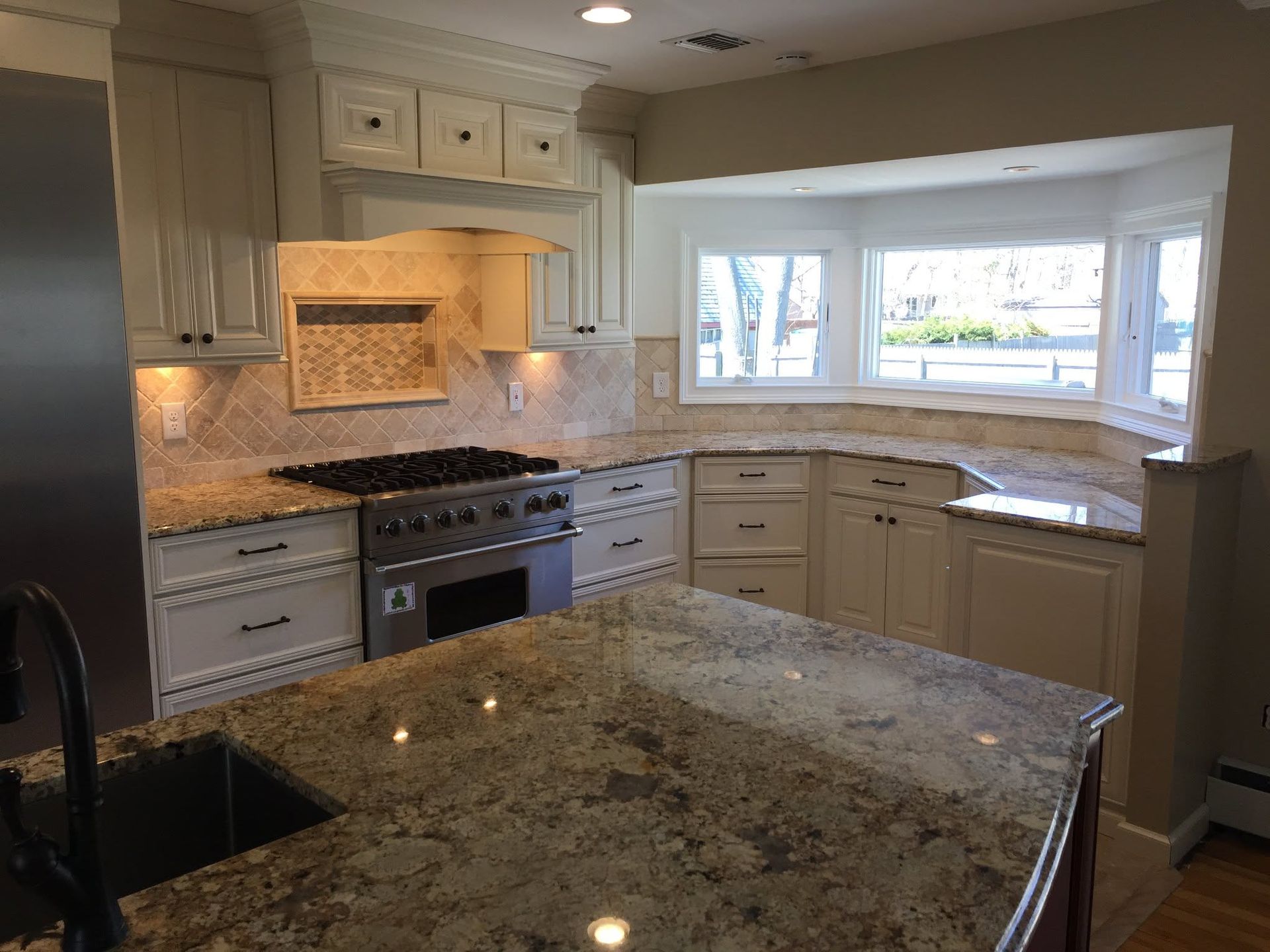 A cream-colored kitchen featuring an island, granite countertops, a gas range, and a bay window.