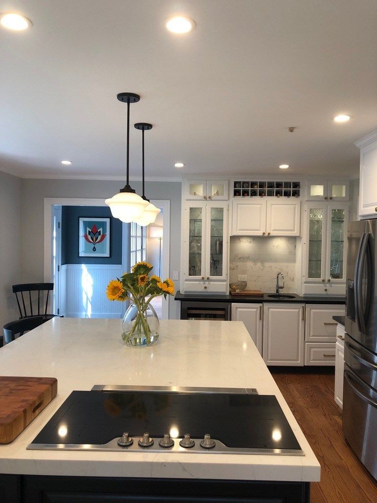 A bright kitchen island with a stovetop and a bouquet of sunflowers, featuring white cabinets and a dark doorway beyond.