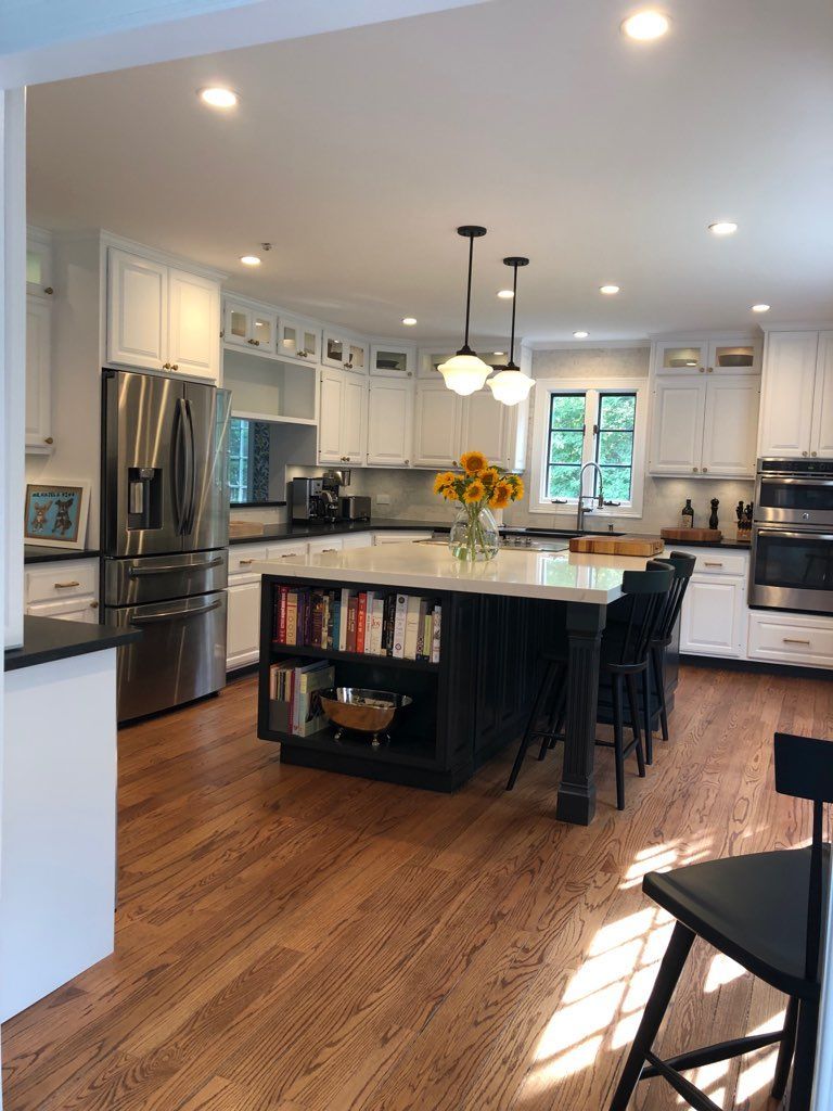 A white kitchen with a dark central island, stainless steel appliances, light countertops, and wooden floors.