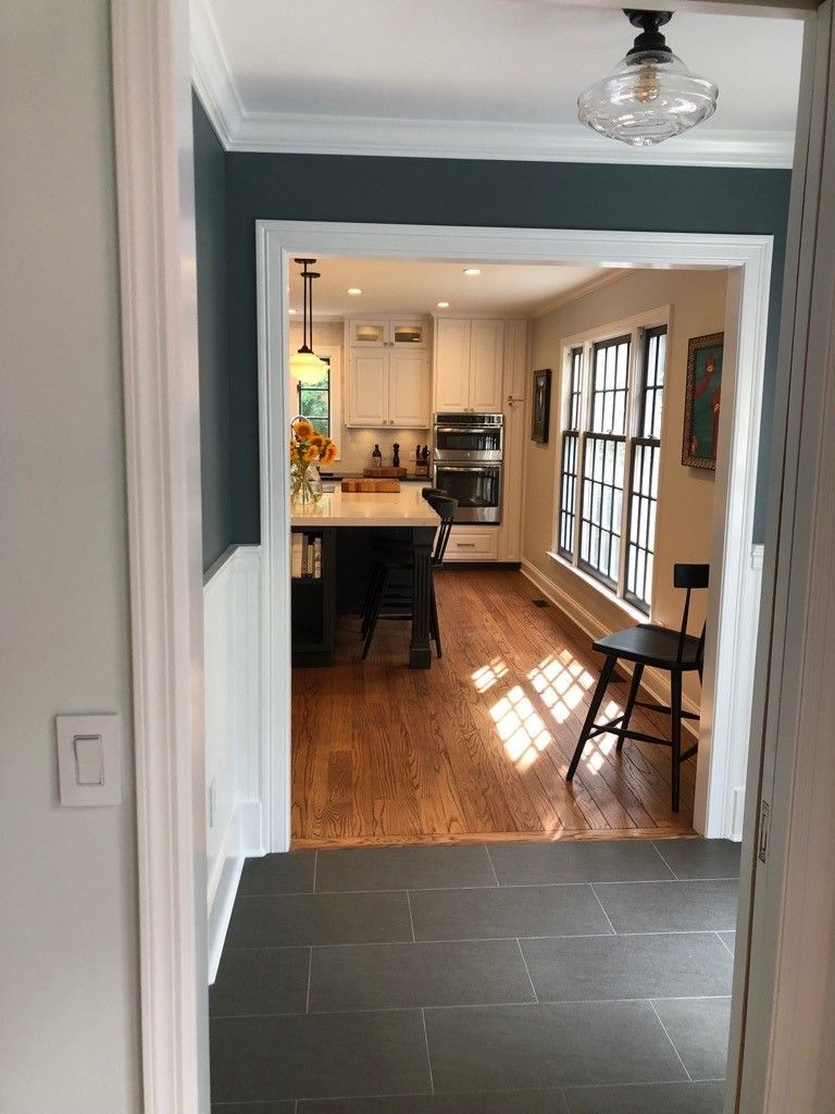 A doorway view into a kitchen with dark charcoal walls, white cabinets, a central island, and wood floors.