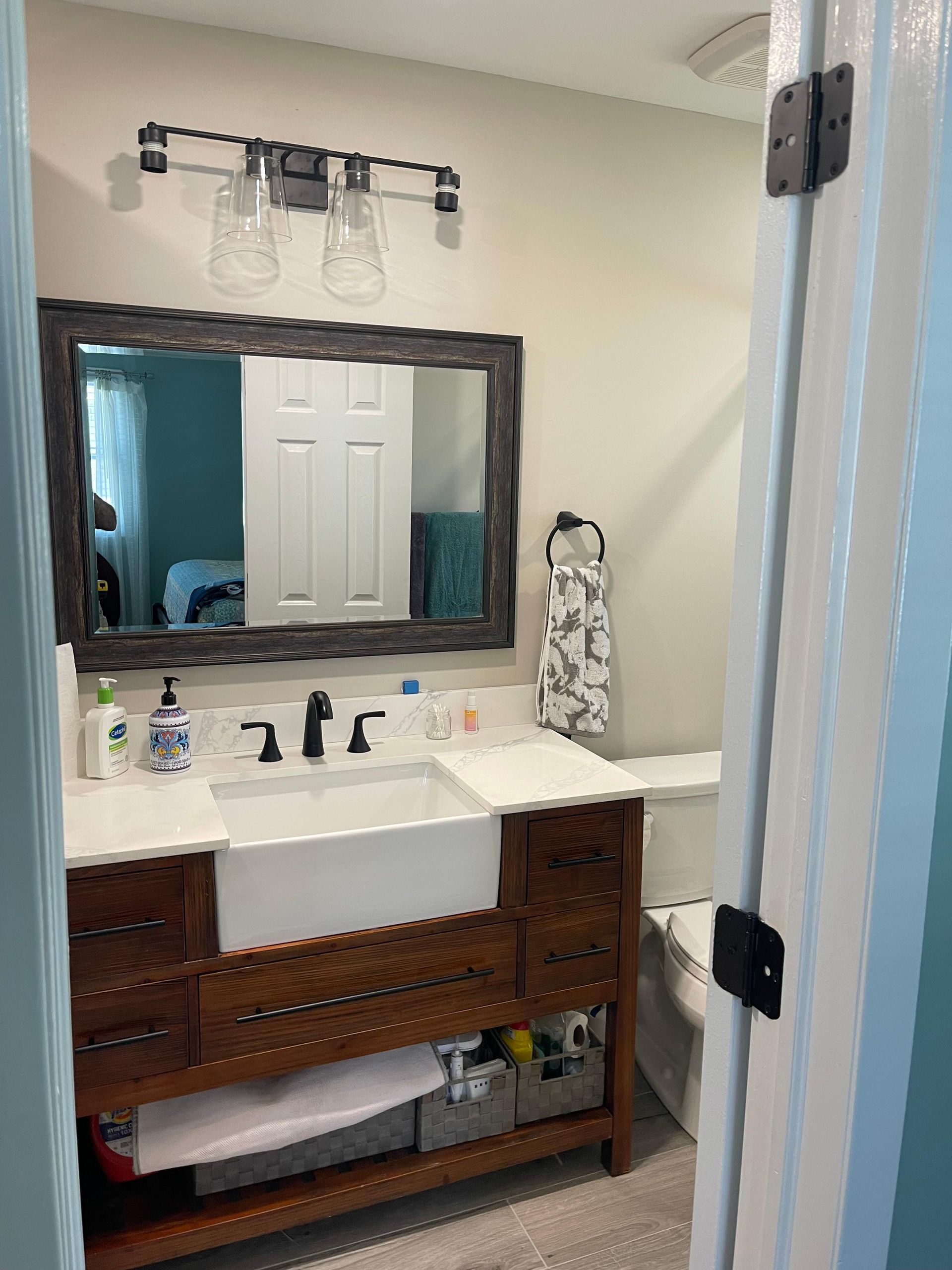 A bathroom featuring a rustic wood vanity with a white farmhouse sink, framed mirror, and two-light industrial wall lamp.