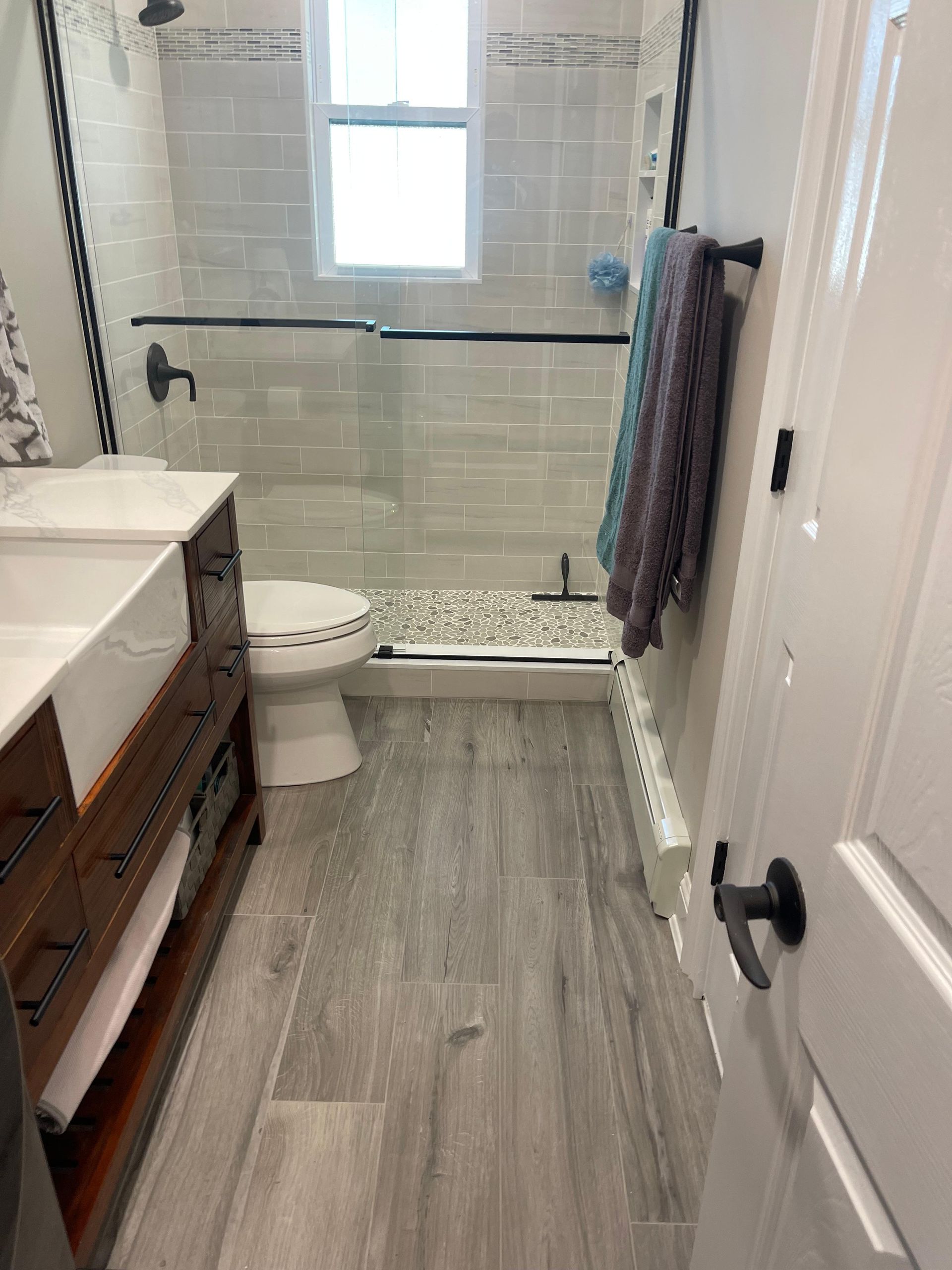 A bathroom featuring a rustic wood vanity, gray wood-look flooring, a toilet, and a glass-enclosed shower with tiled walls.