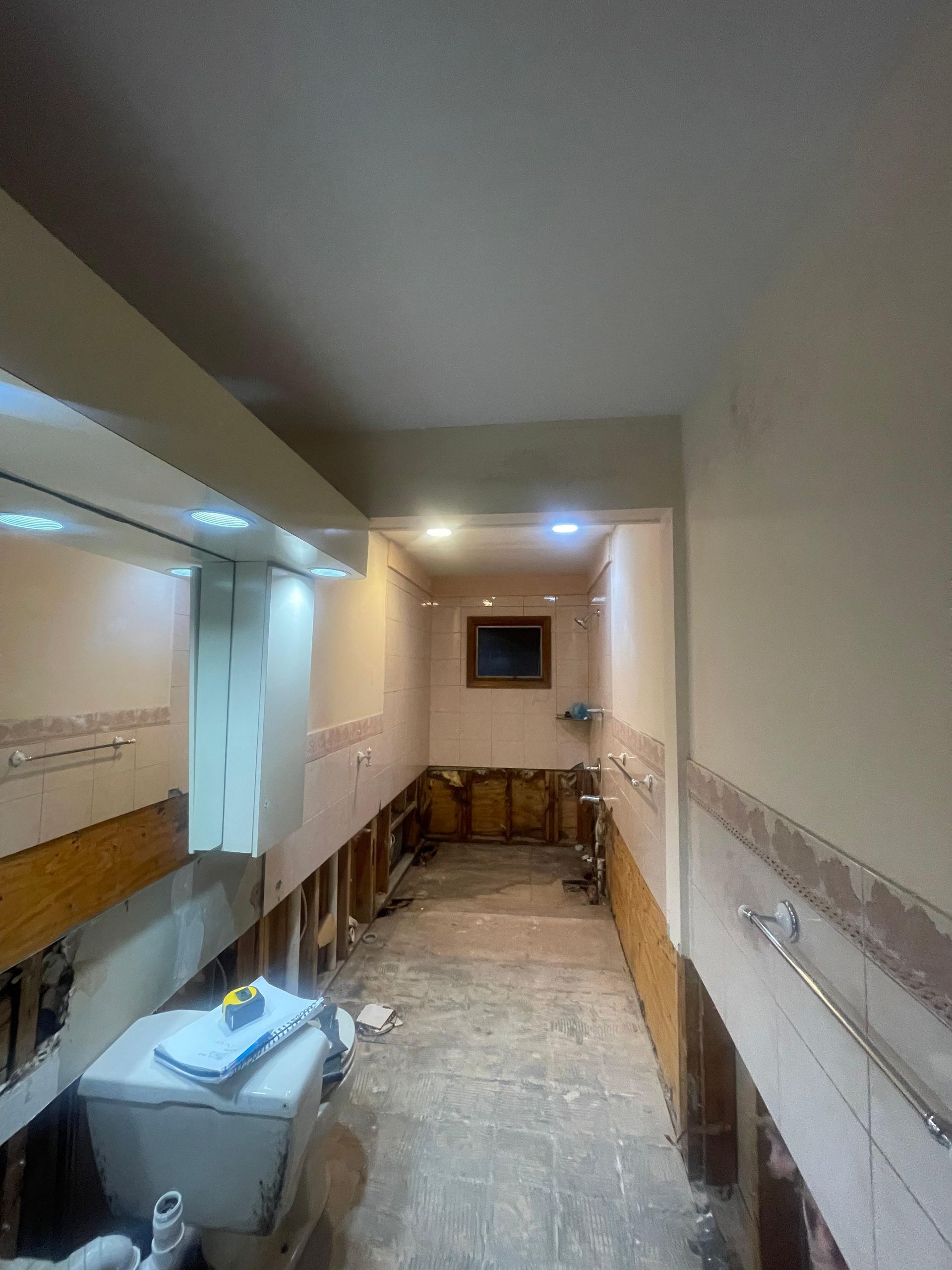 A narrow, unfinished bathroom hallway with exposed wooden framing along the walls, beige paint, and a tiled floor.