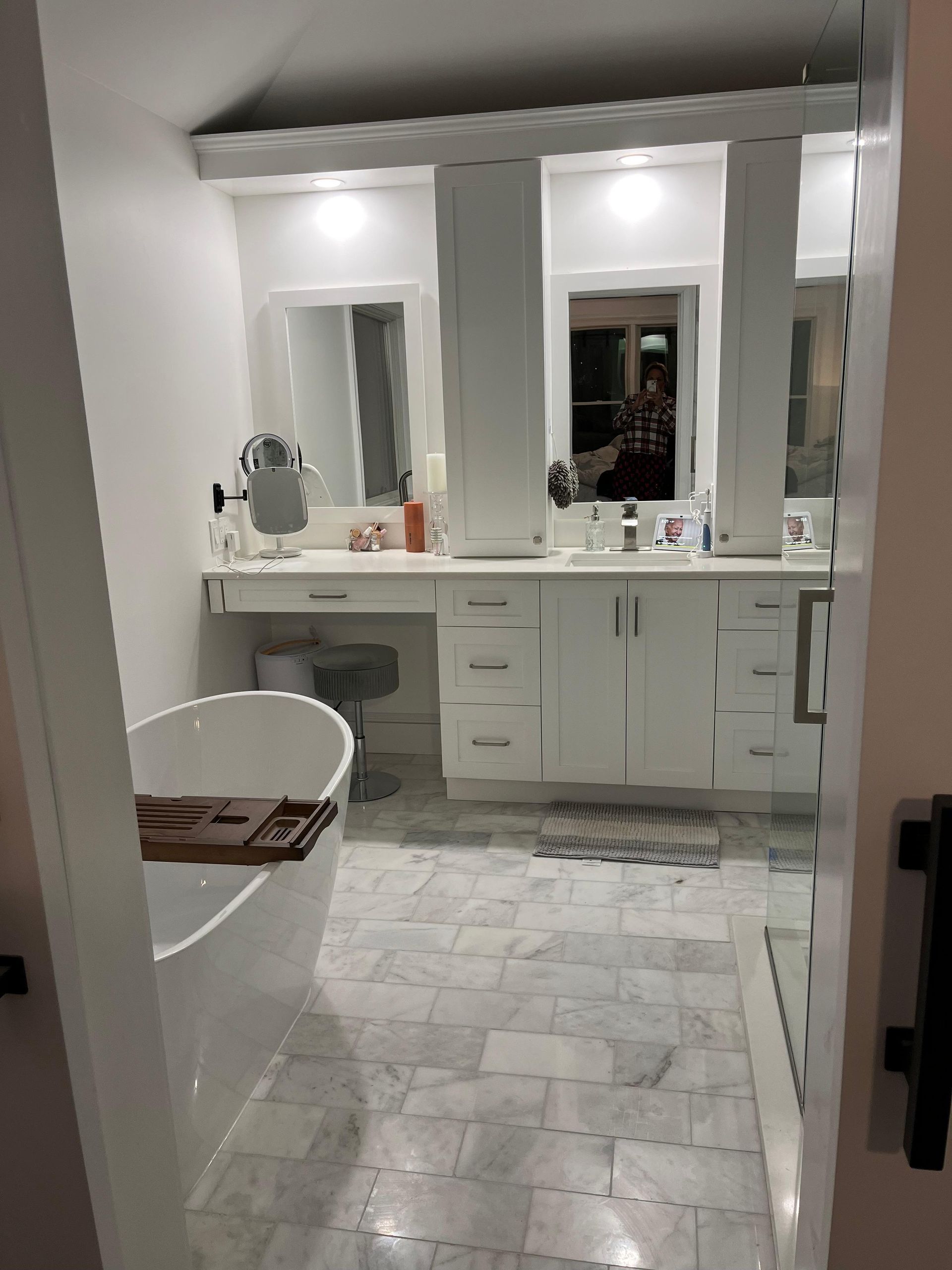 A white bathroom with a freestanding tub, a marble tile floor, a double vanity with mirrors, and a vanity makeup station.