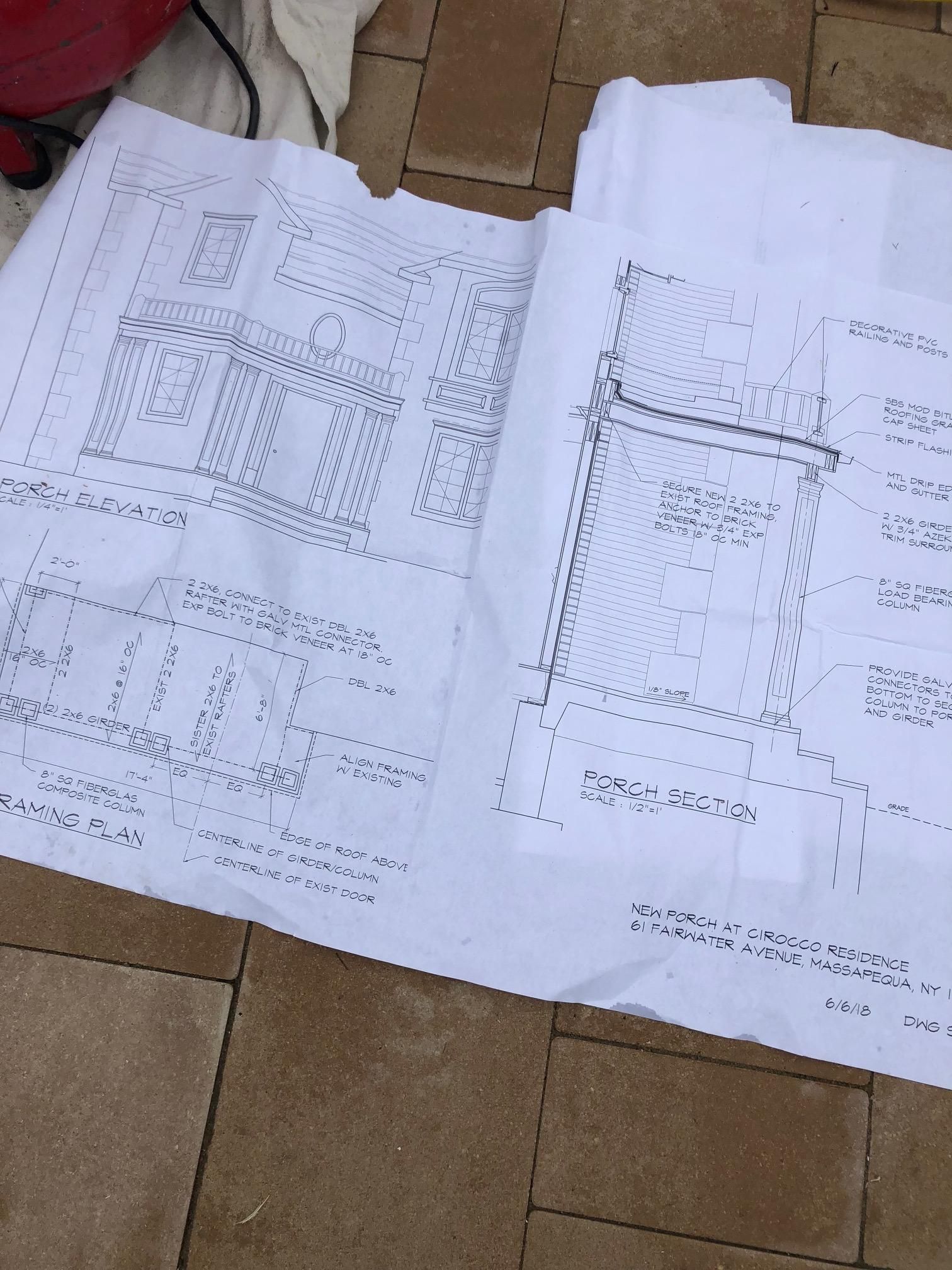 Blueprints laid flat on a paved outdoor surface, showing structural designs and building plans.