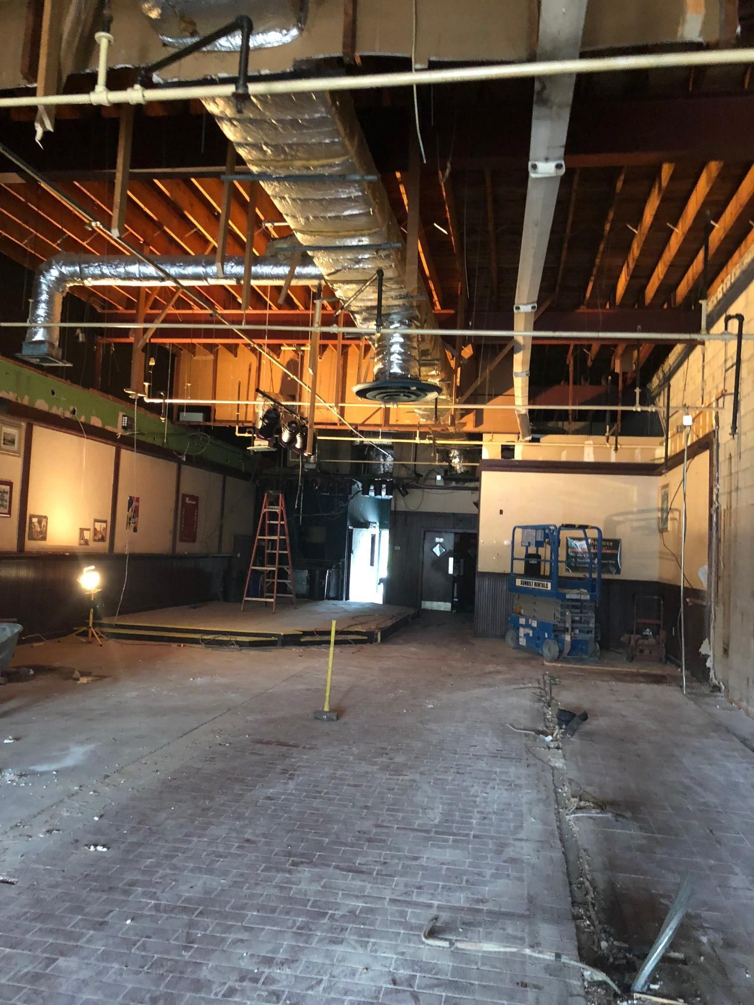 An interior view of a room under construction with exposed wooden ceiling beams, metal ductwork, and equipment.