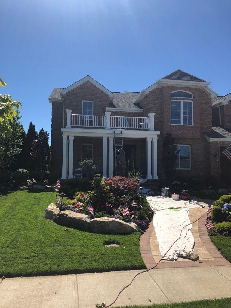 A large brick house with a white front porch and balcony, with a canvas drop cloth spread across the front walkway.