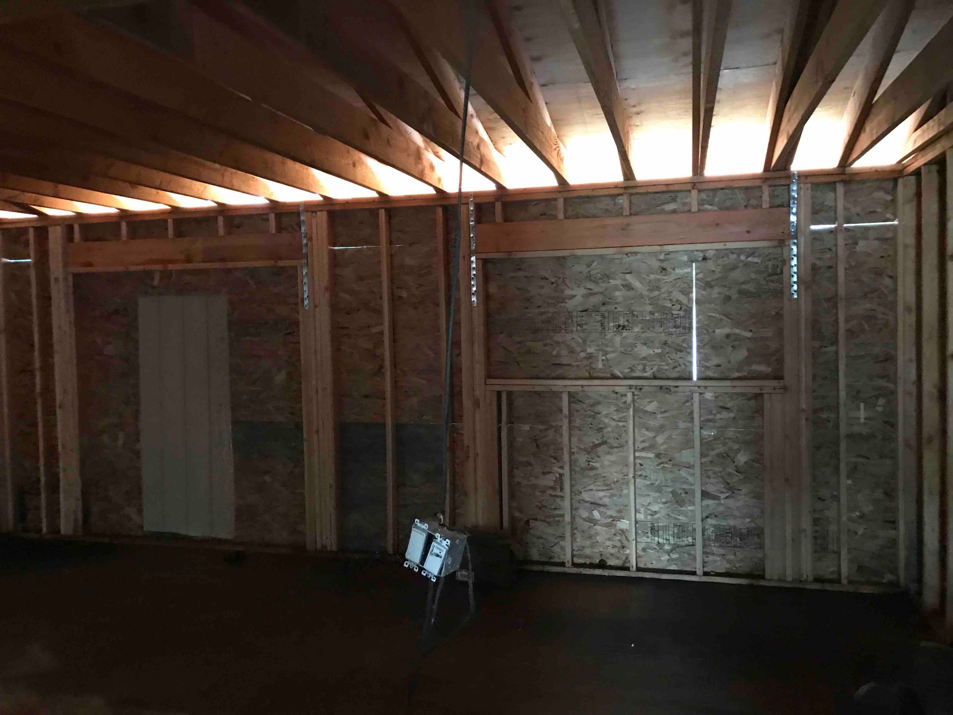 Framed wall interior under construction with exposed wooden studs, joists, and OSB panels.