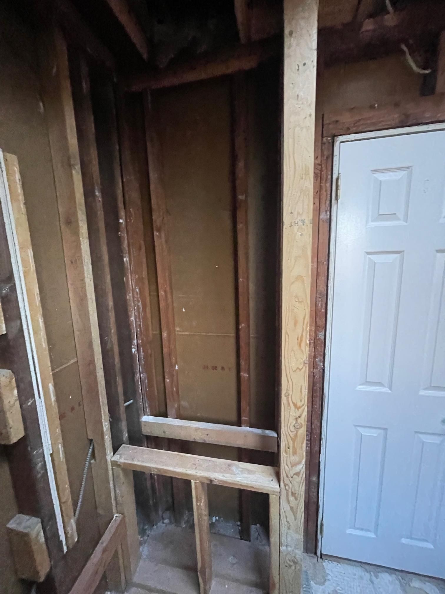 An unfinished interior space showing exposed wooden wall framing and a white door in a home renovation setting.