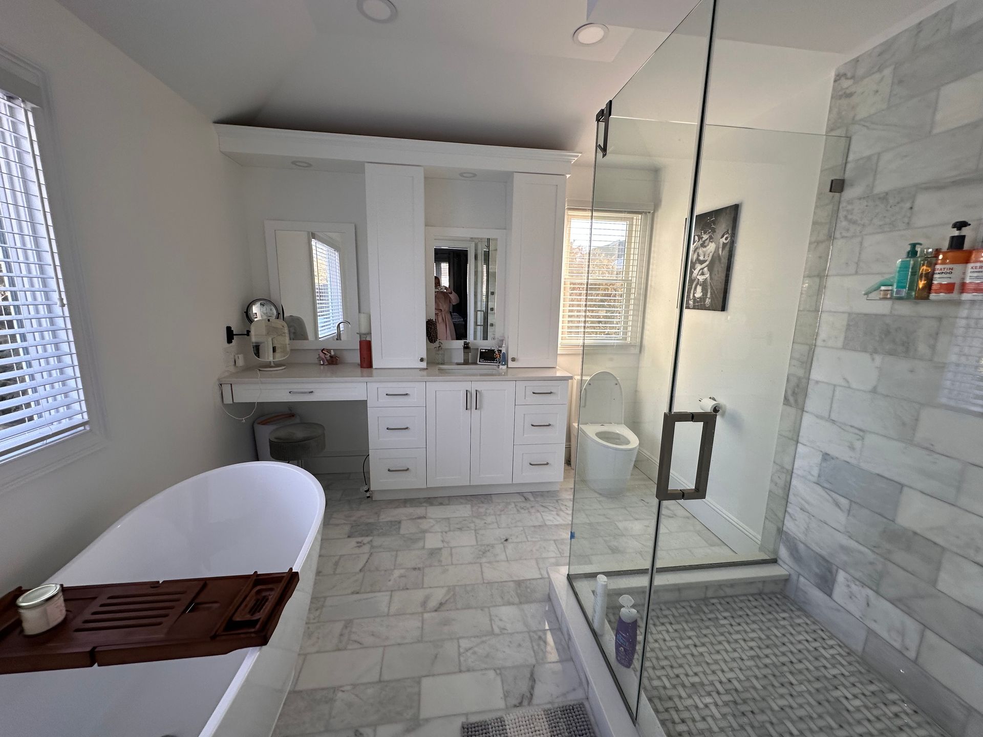 A modern bathroom featuring a white vanity, a freestanding tub, a walk-in glass shower, and gray and white marble tiles.