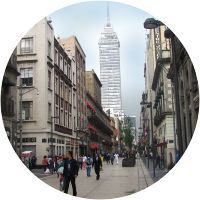 Una calle de la ciudad con un edificio alto al fondo y gente caminando por ella.