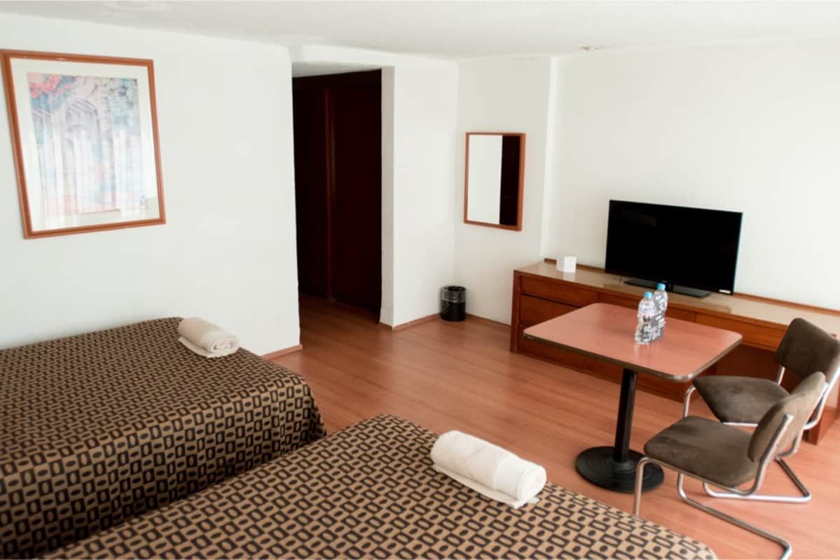 Una habitación de hotel con dos camas, una mesa, sillas y un televisor de pantalla plana.