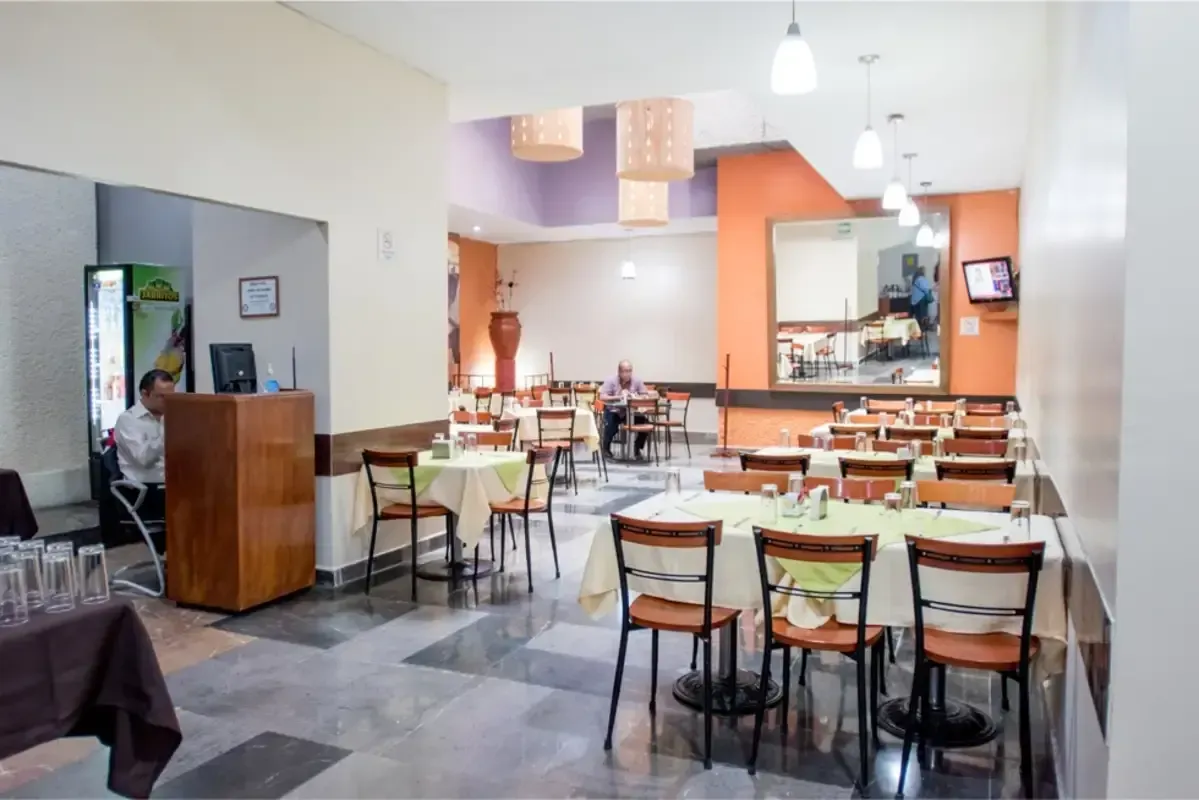 Un restaurante con mesas y sillas y un hombre sentado en un podio.