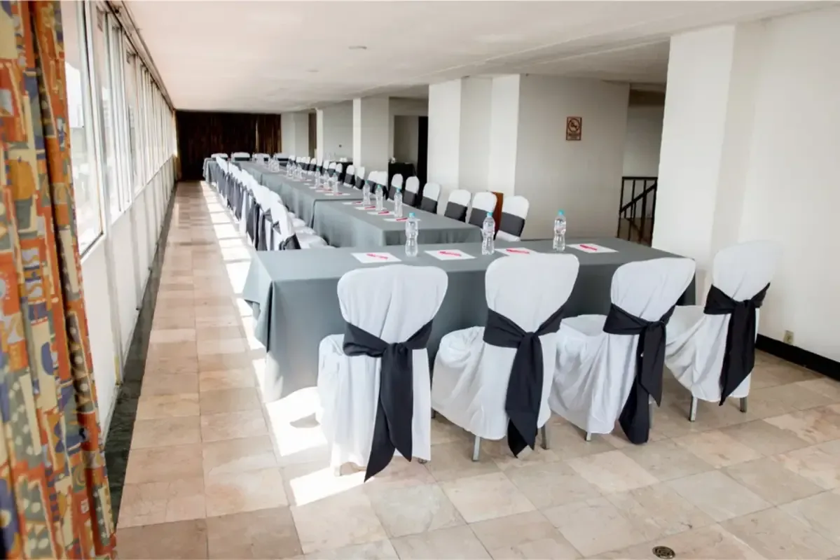 Una sala larga con mesas y sillas preparadas para una reunión.