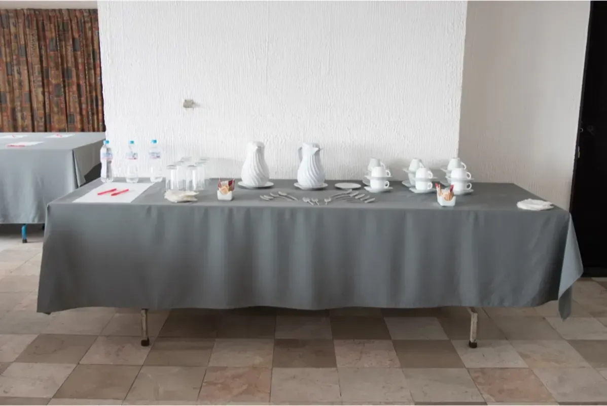Una mesa larga con un mantel gris y platos y tazas sobre ella.