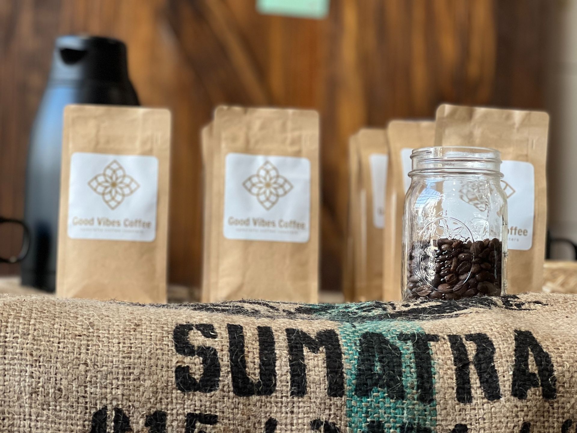 Coffee bags and a jar of beans behind a burlap sack labeled “SUMATRA”