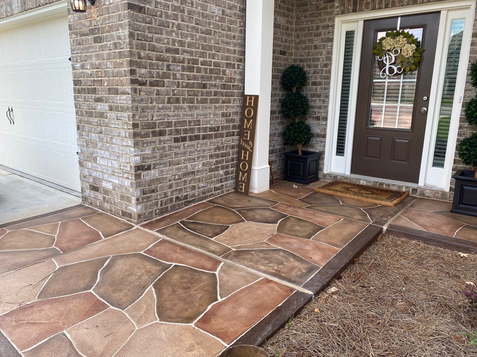 Front porch with stone walkway, brown double doors, and a white garage beside a brick exterior.