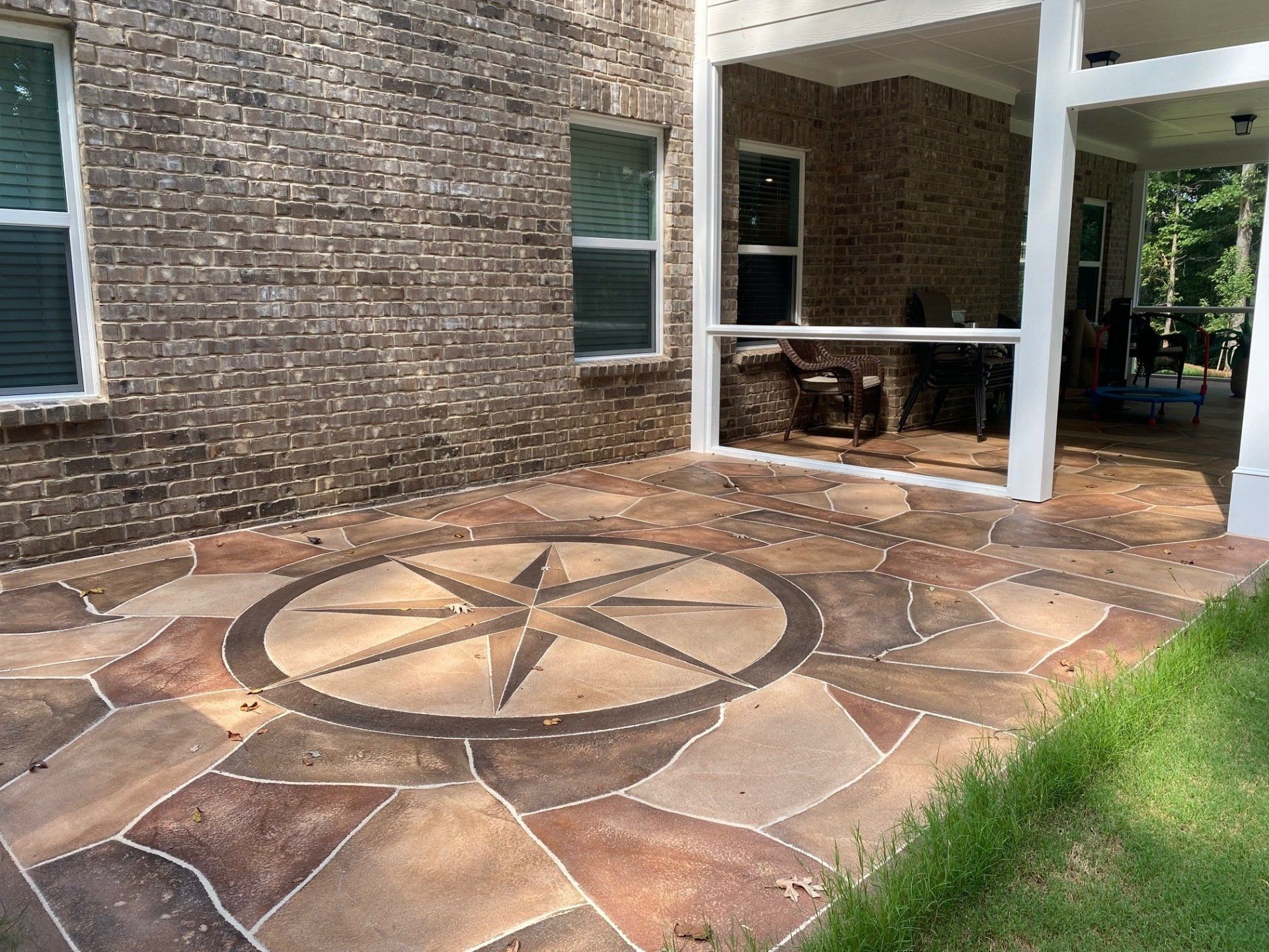Stone patio with a compass rose design beside a brick house and covered outdoor seating area