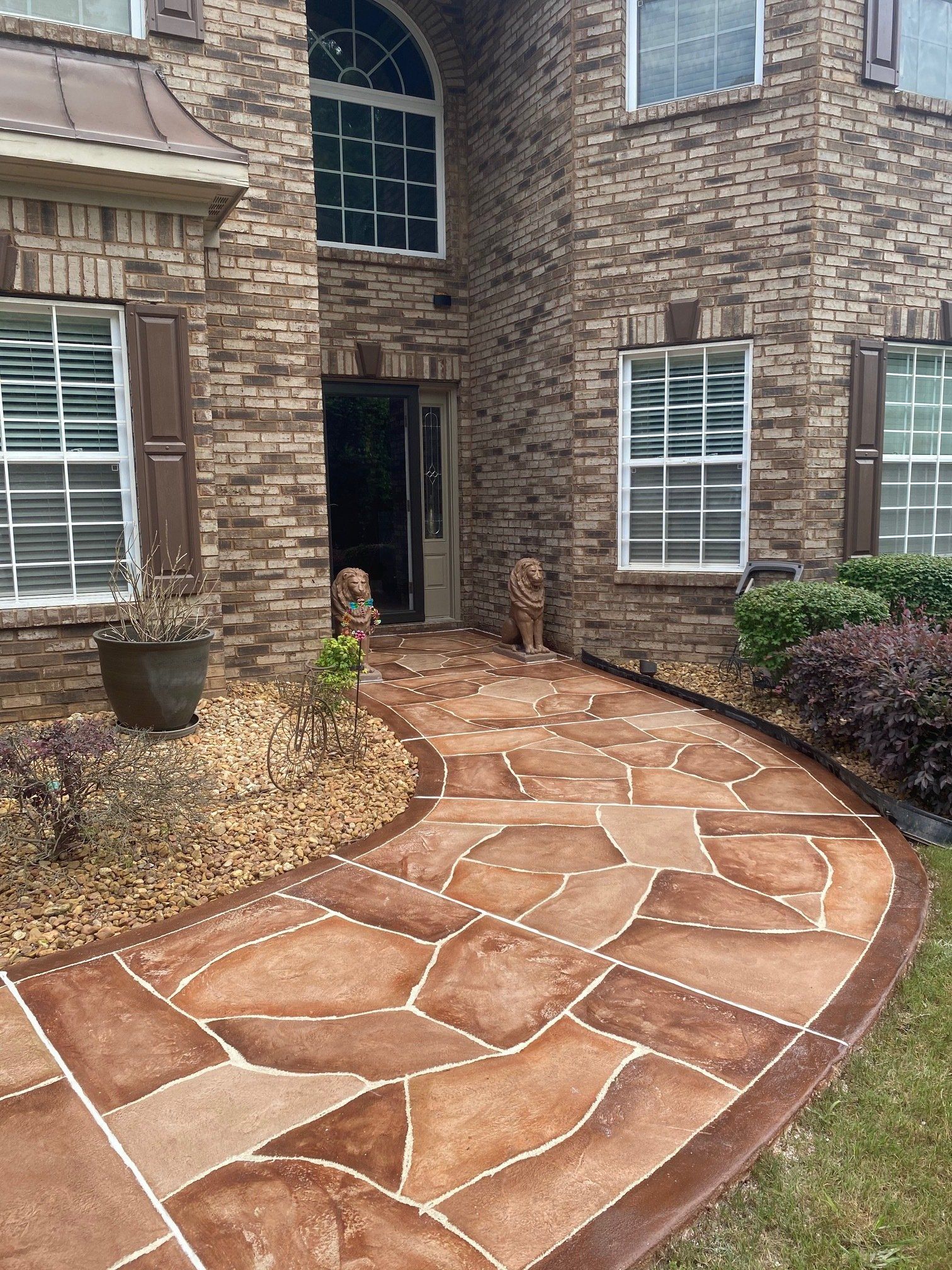 Curved stone walkway leading to a brick house entrance with a potted plant and windows