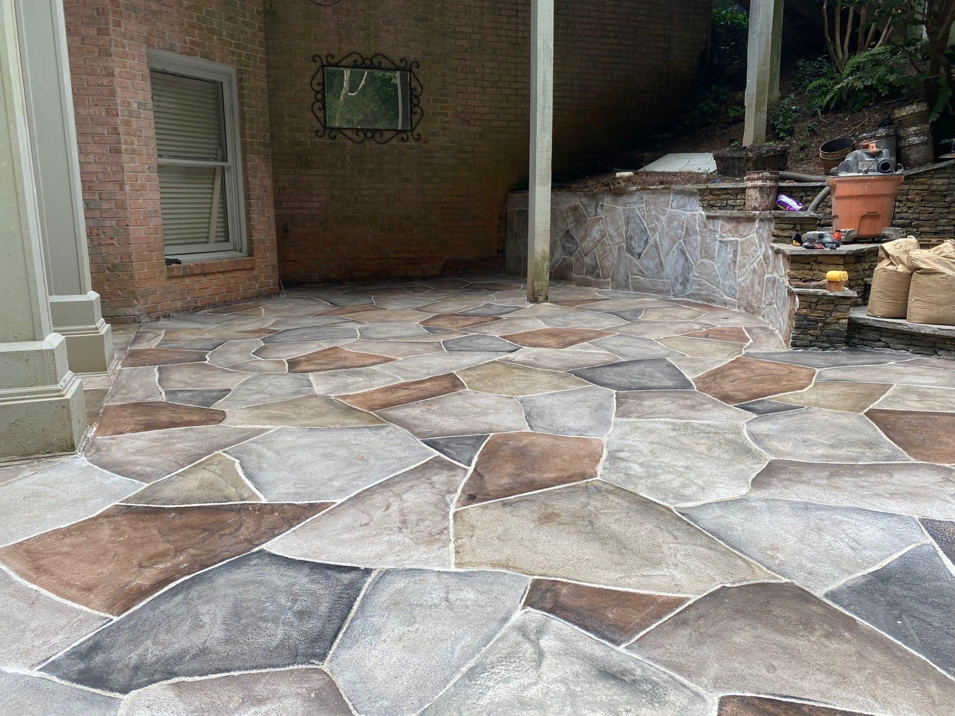 Stone patio with irregular beige and gray pavers beside a brick wall and small fountain area