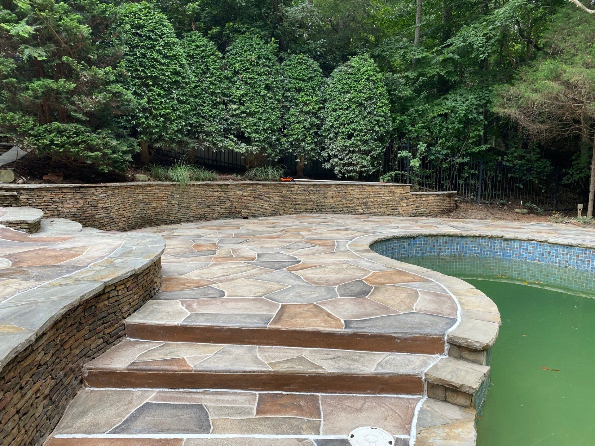 Stone patio beside a green-tinted pool in a lush garden setting