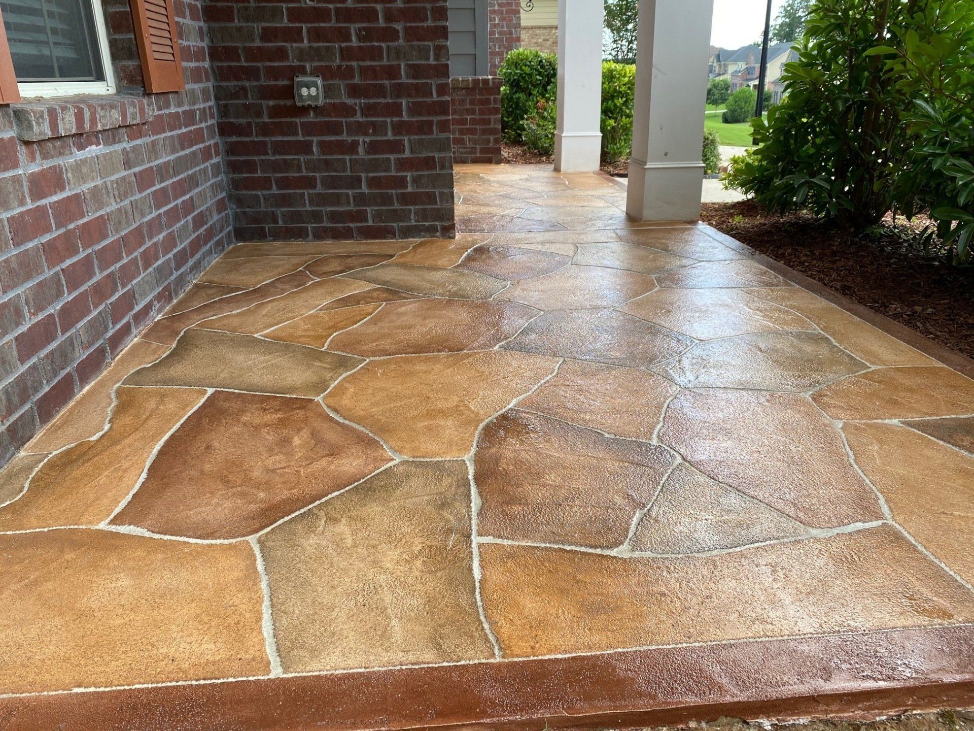 Stone walkway with wet tan flagstones beside a brick house and columns