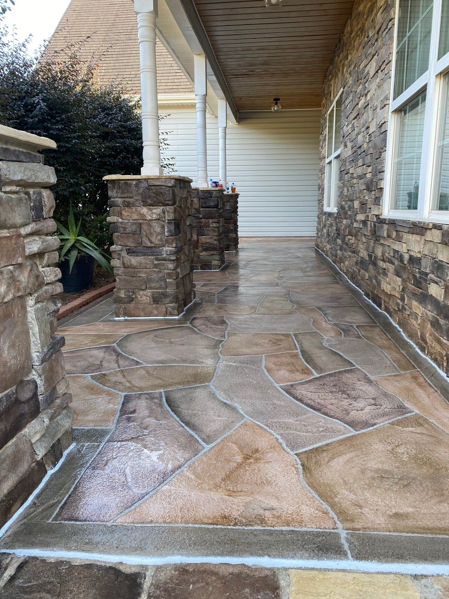 Stone-front porch with irregular stone walkway, brick columns, and white siding under a covered roof.