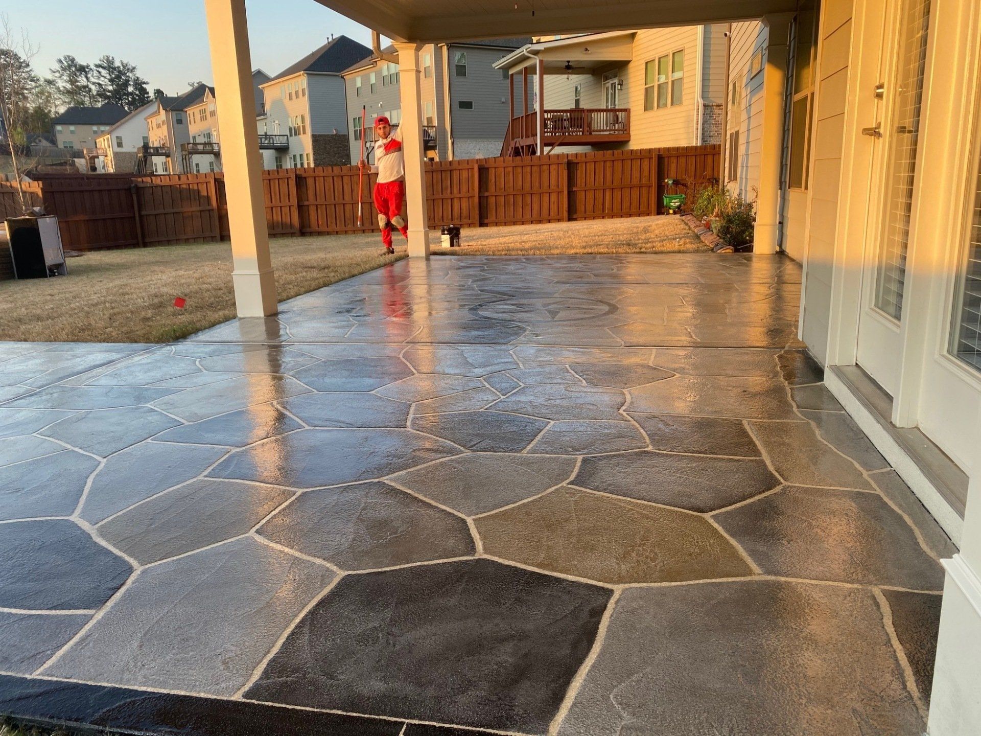 Stone patio with a child in red near a backyard fence at sunset