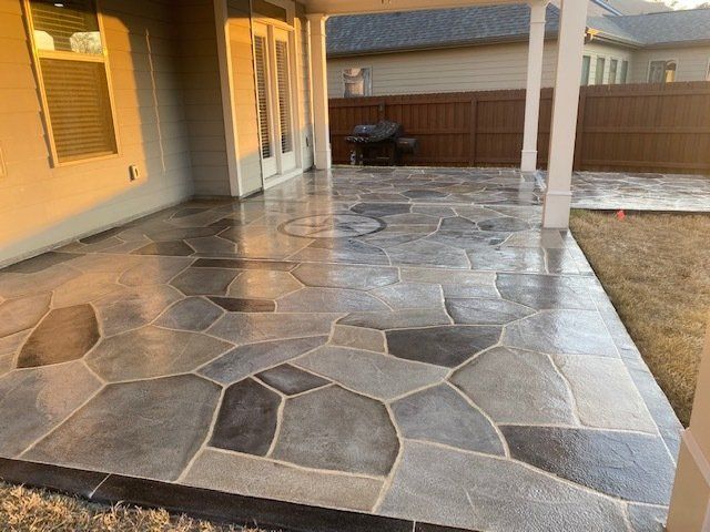 Covered patio with stamped stone flooring, beige columns, and a fenced backyard beyond