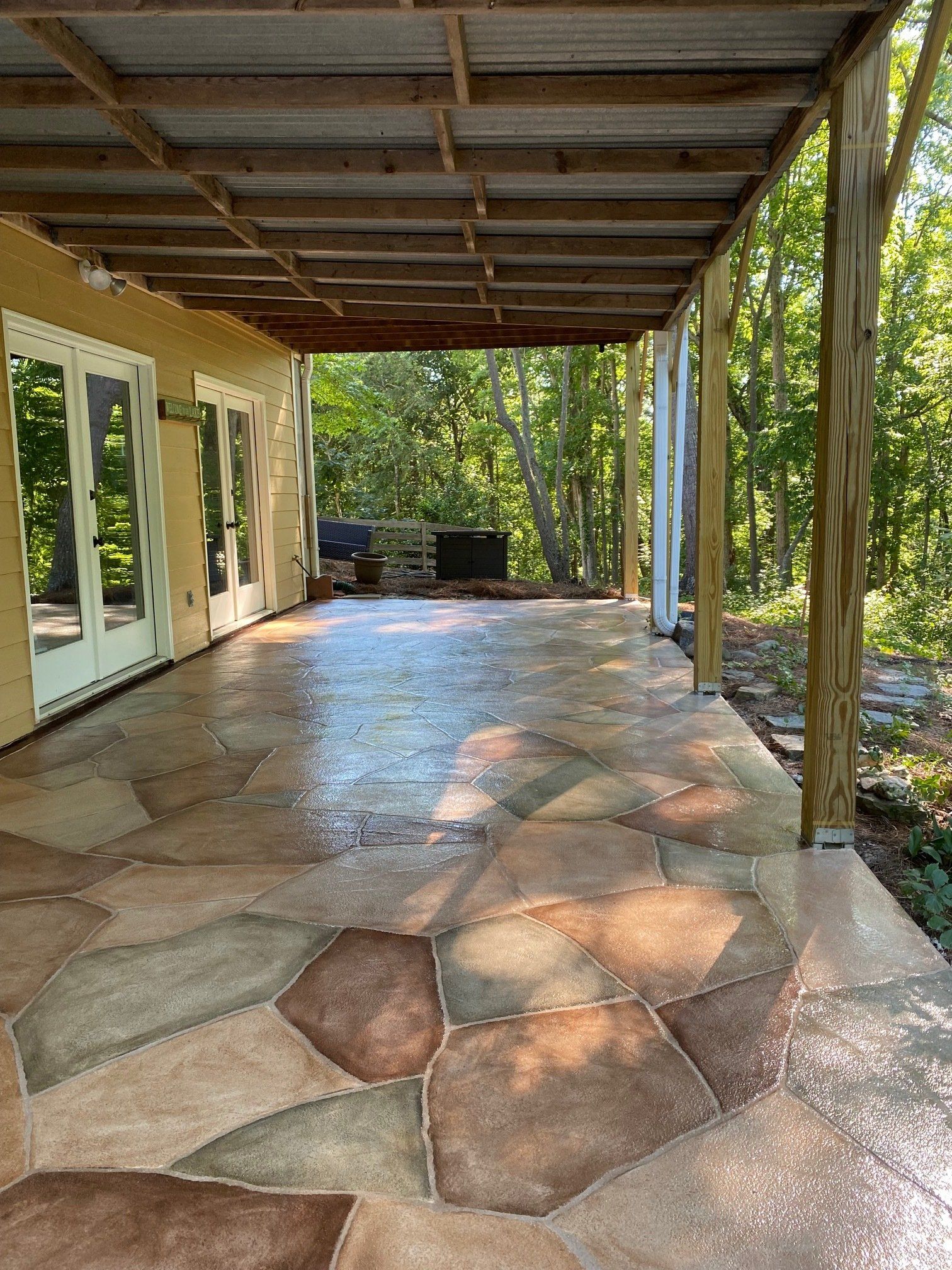 Stone patio under a covered porch with glass doors and trees beyond