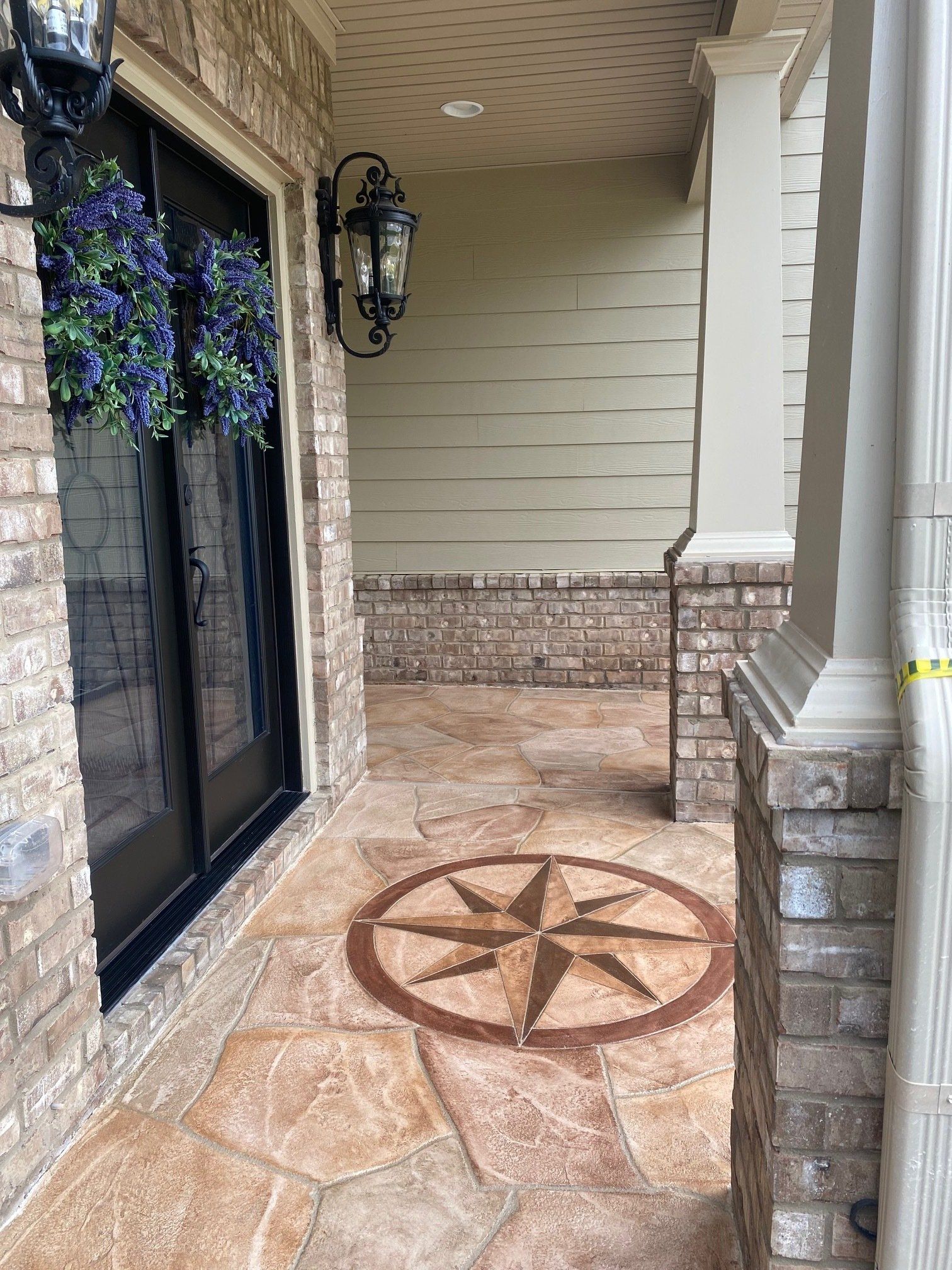 Front porch with stone flooring, black door, lantern, and decorative compass rose inlay on the ground