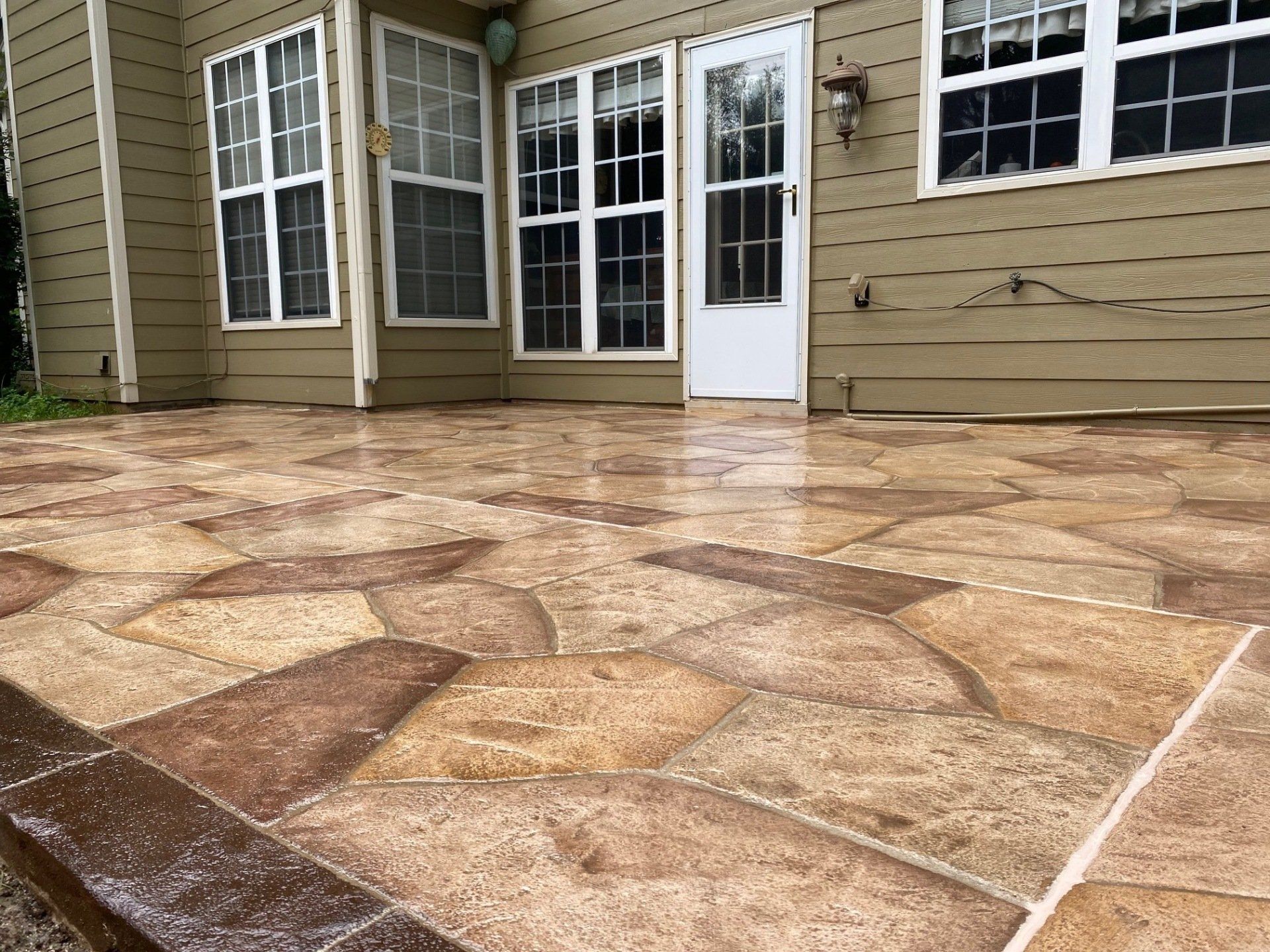 Stone patio in front of a tan house with white doors and windows