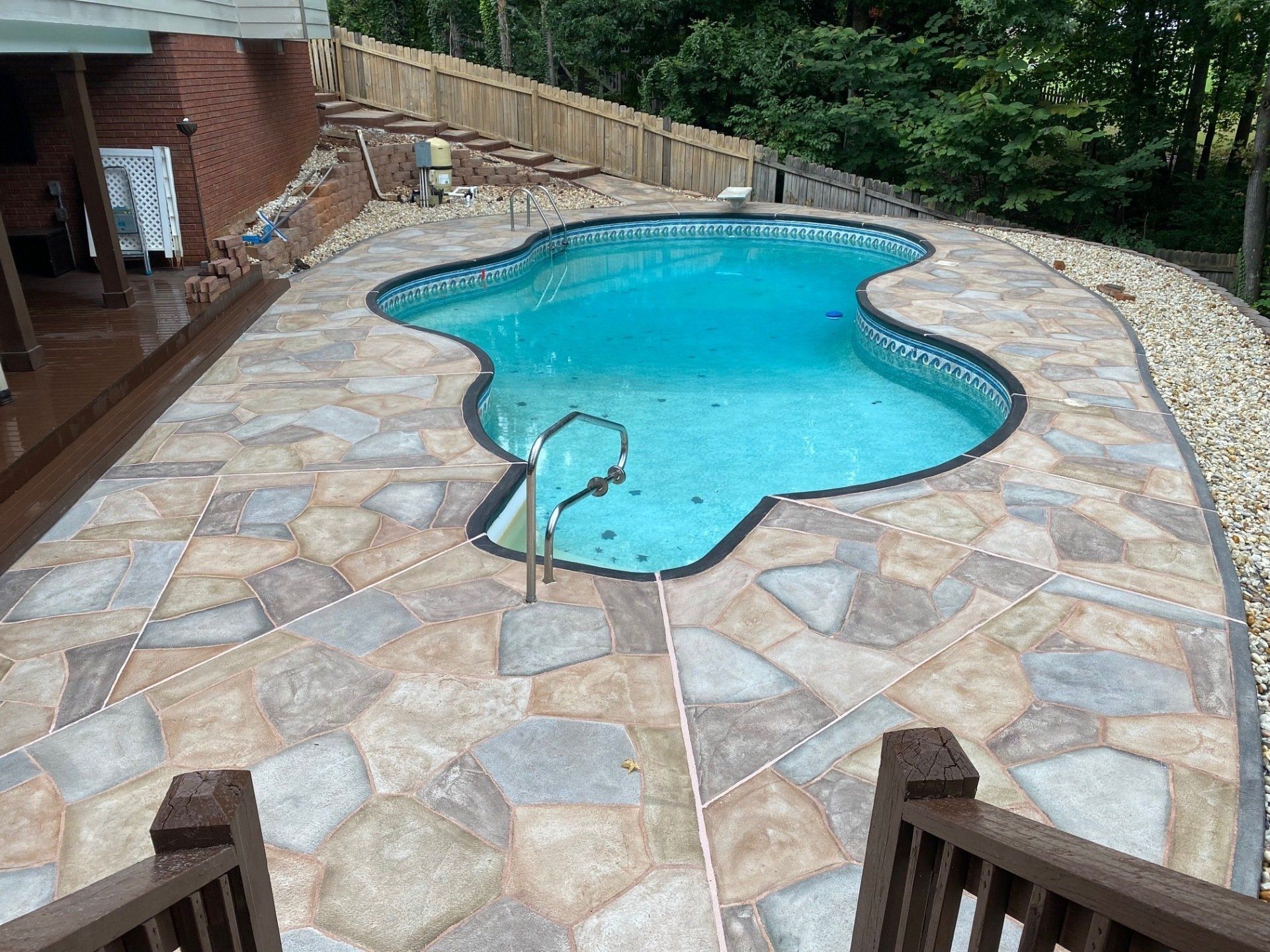 Backyard swimming pool with stone patio, turquoise water, and stairs descending into the water