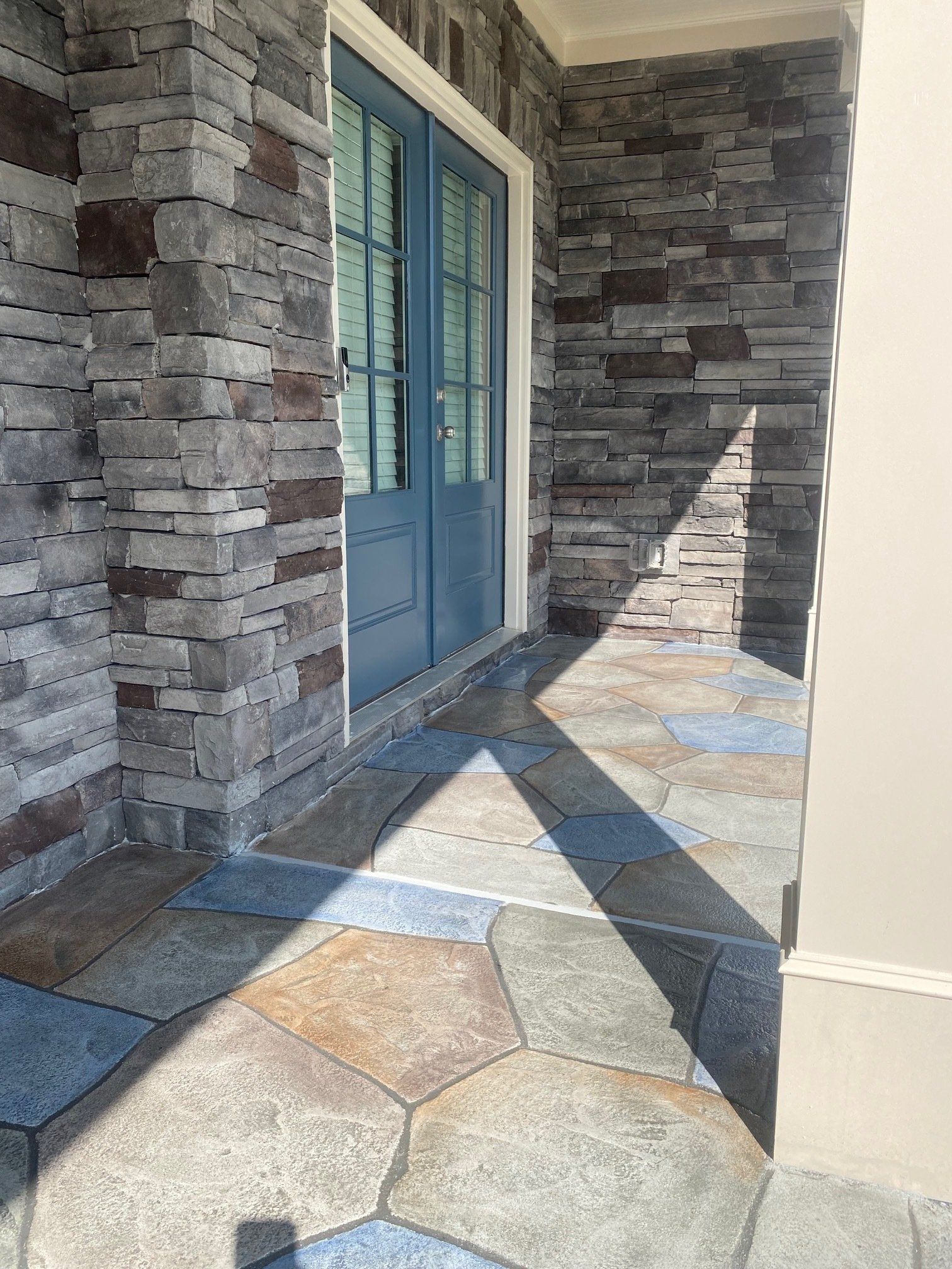 Front porch with blue door, stone columns, and patterned tile floor in sunlight