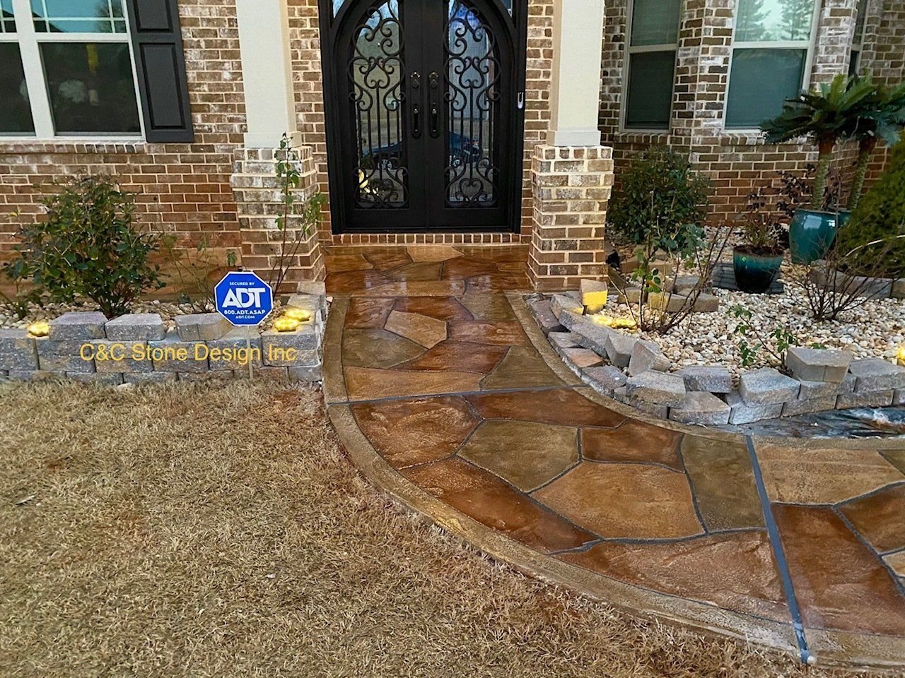 Front walkway with wet stone pavers leading to a brick house entrance and black double doors.