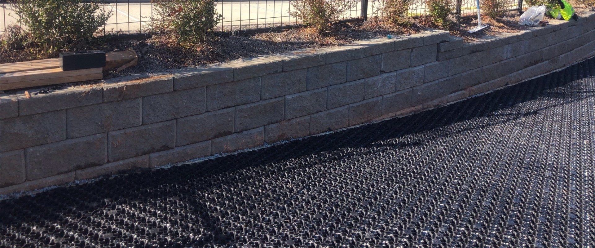Raised stone planter beside a gravel path, with sparse desert plants in sunlight.