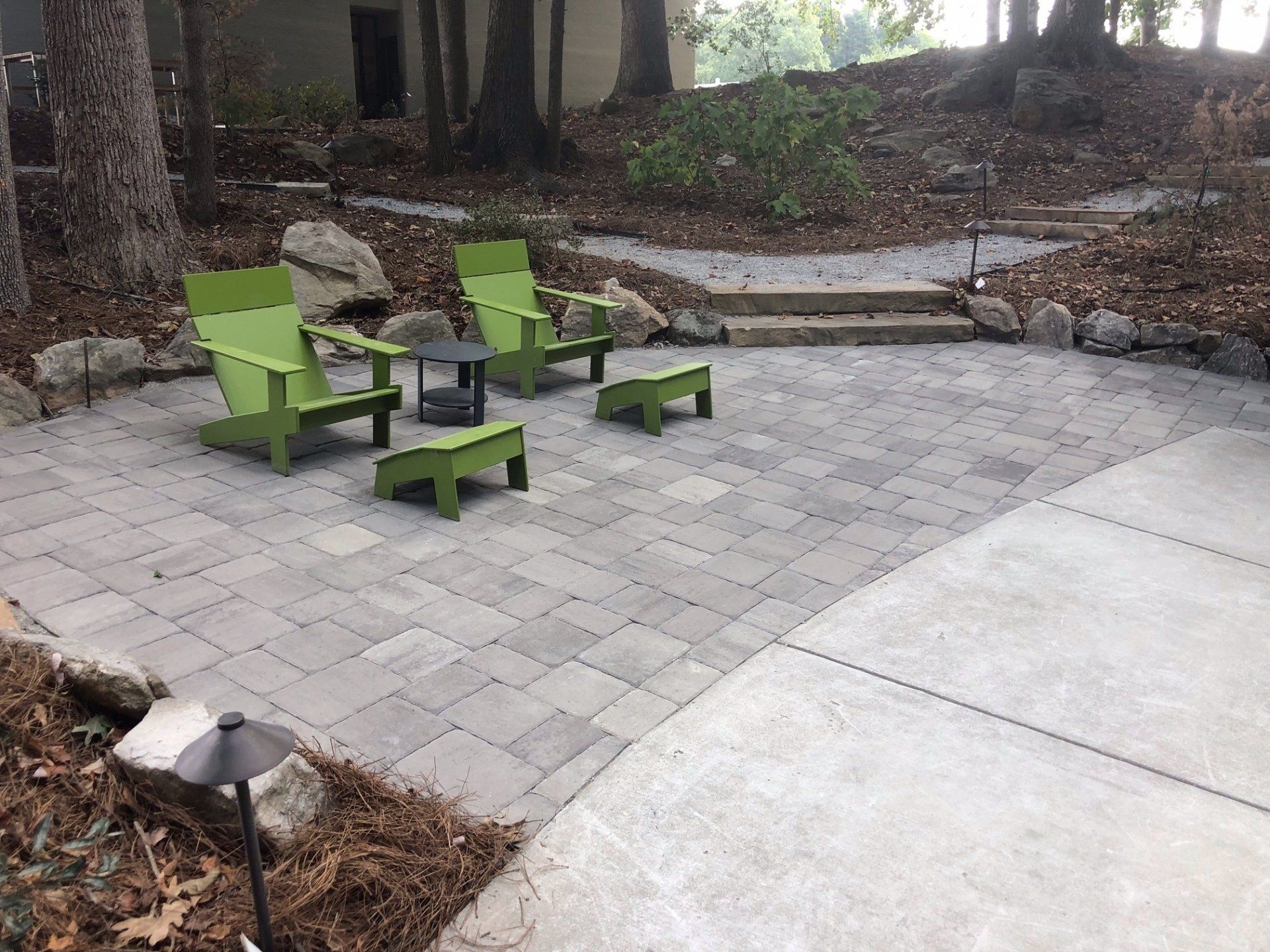 Green patio furniture on a paved courtyard beside a curved walkway and trees