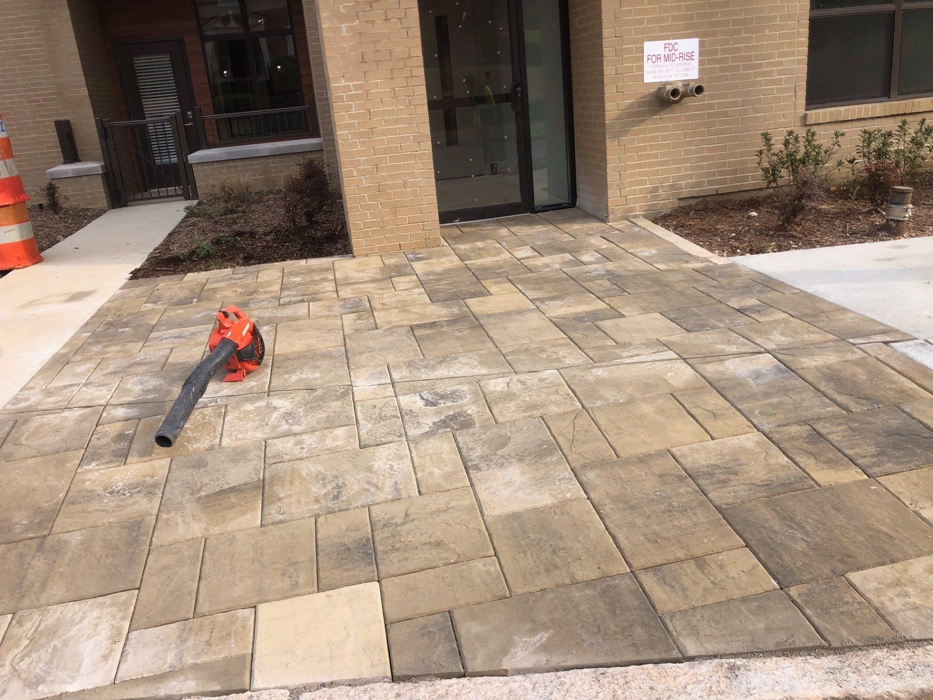 Patio with stone pavers beside a building entrance, with a red leaf blower on the ground