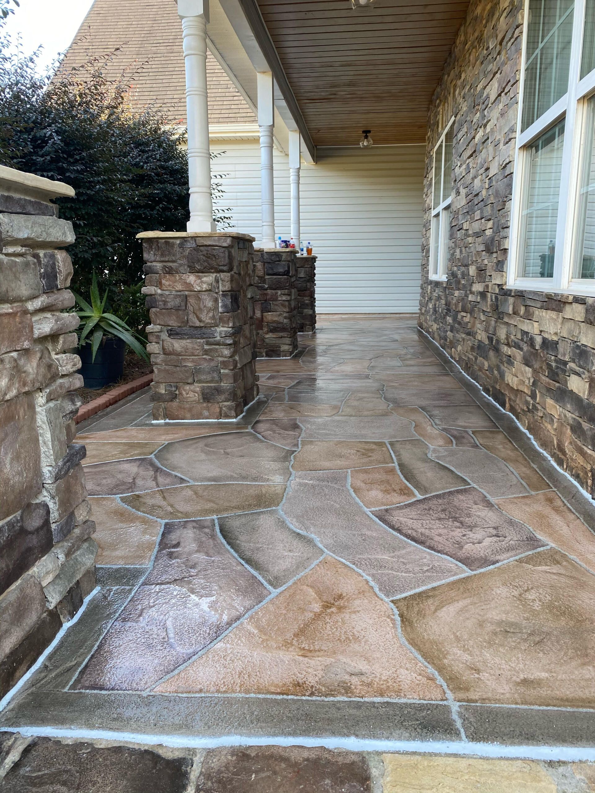 Stone walkway beside a house with white siding, covered porch, and brick columns