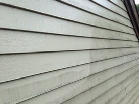 Close-up of beige siding on a building, partially cleaned, showing the contrast between dirty and clean.