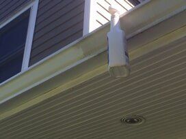 Spray bottle hanging on a white gutter on a house.