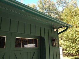 Green building with gutter, security lights, and garage door.