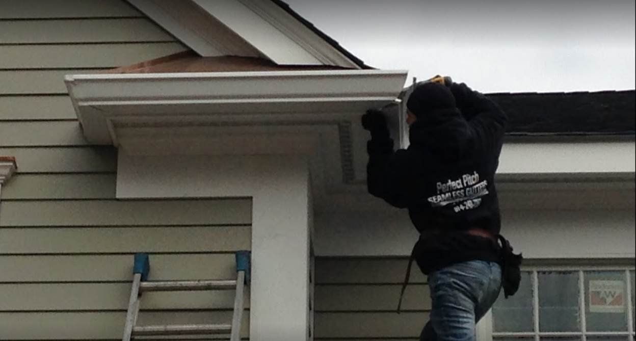 Person on ladder installing gutter on a light green house.