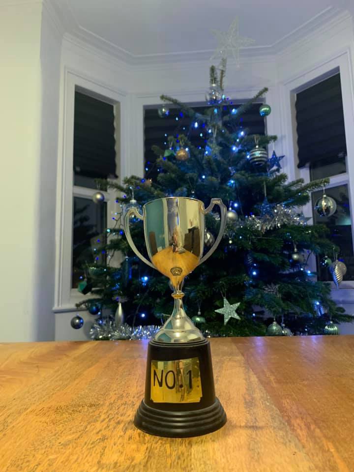 Silver trophy with “No. 1” on base, in front of decorated Christmas tree.