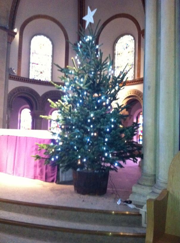 Christmas tree with white lights and star on top, in a church. Purple fabric in the background.