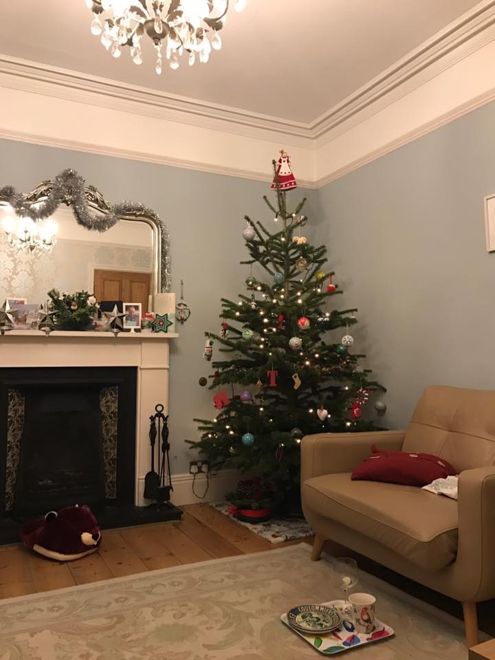 Christmas tree decorated in living room with armchair and fireplace.