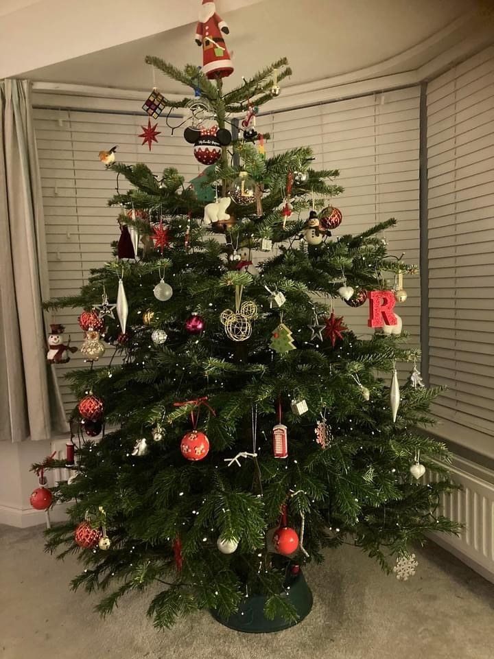 Christmas tree decorated with ornaments, in a room with a window and curtains.