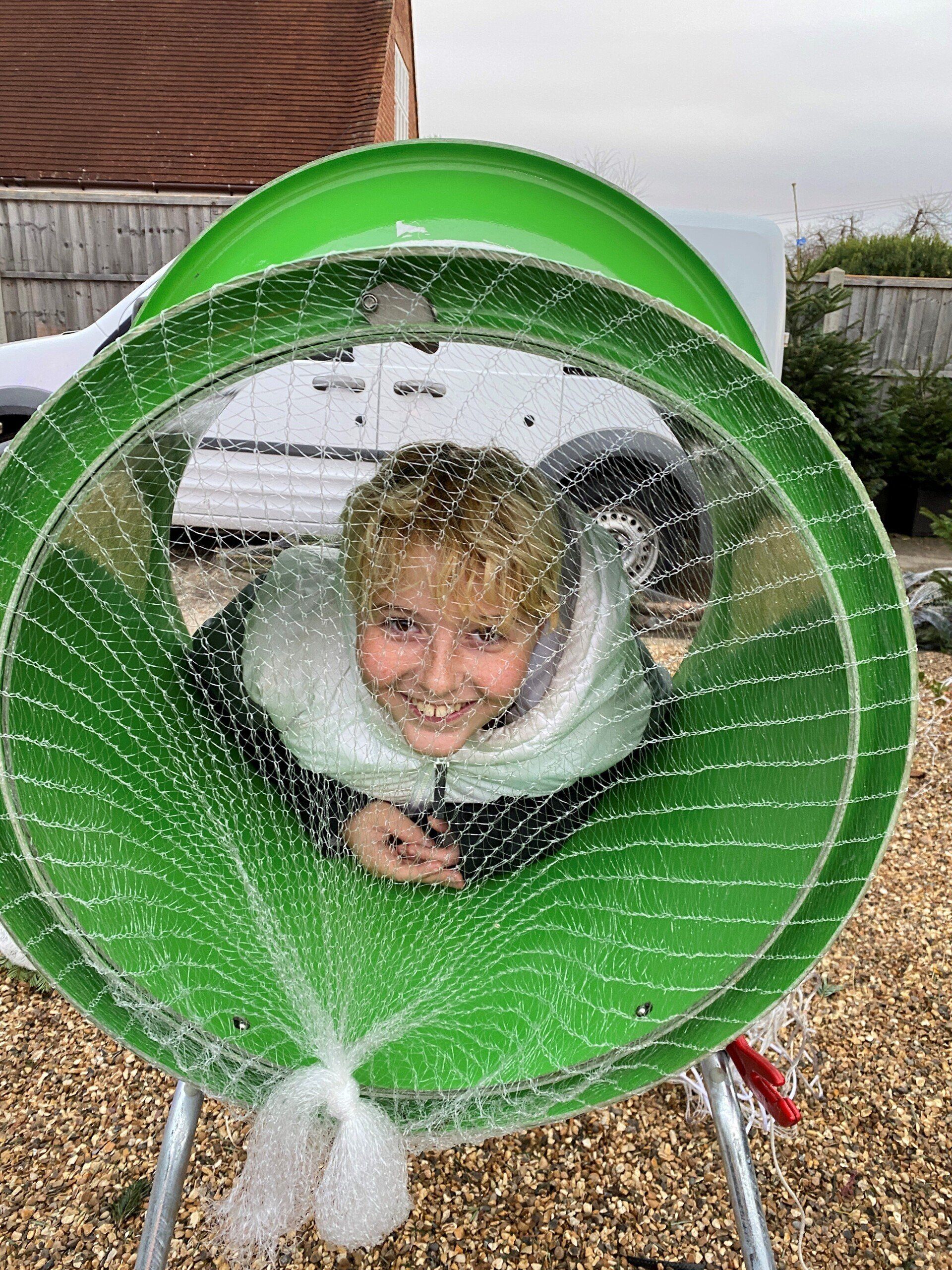 Person smiles through a green tunnel, outdoor setting.