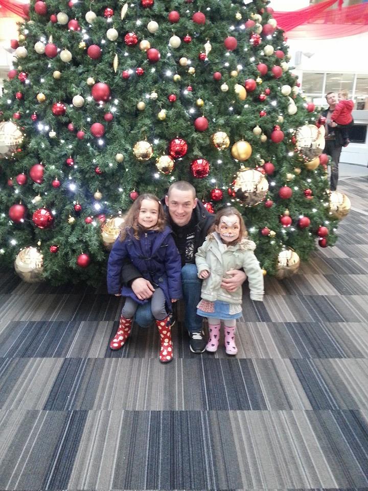 Man and two young children pose in front of a decorated Christmas tree.