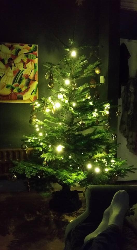 Lit Christmas tree, soft glow, in a cozy, dark room. Person's feet up in foreground.